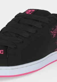 Gros plan d'une basket noire avec des logos roses, des lacets noirs, des motifs paisley roses et une semelle blanche avec une bande rose.