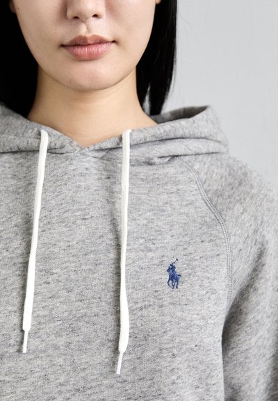 Grijze katoenen hoodie met een gestructureerde afwerking, voorzien van witte koordjes en een blauwe geborduurde logo aan de linkerkant.