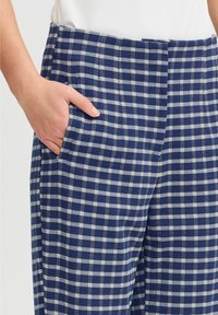 Pantalons à carreaux bleu marine et blancs avec une texture lisse, dotés de poches latérales et d'une coupe droite. Convient pour une tenue décontractée ou formelle.