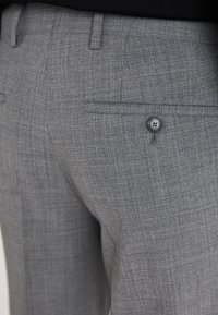 Pantaloni grigi su misura in un tessuto strutturato. Include una tasca posteriore con un bottone nero e un frontale piatto con passanti per la cintura.