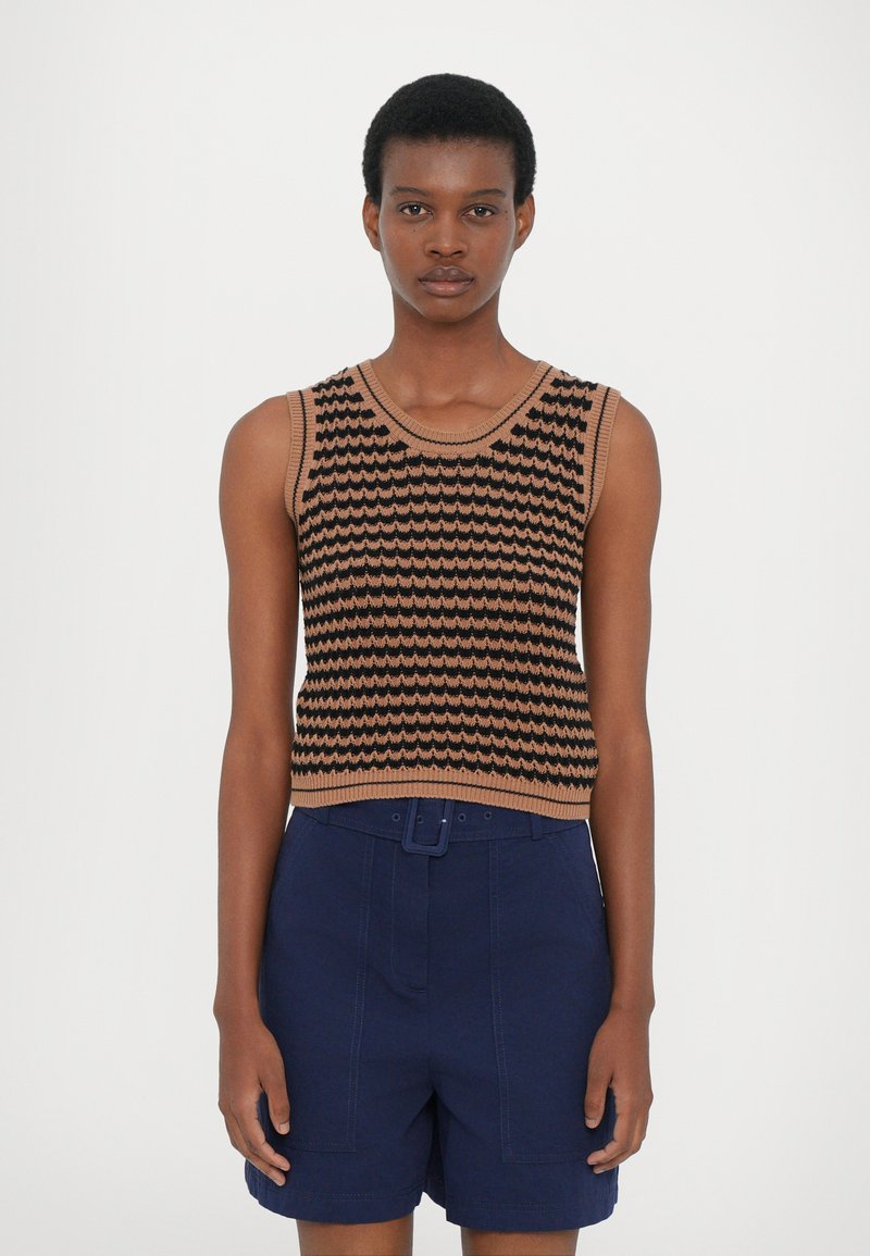 Braun und schwarz gestrickter ärmelloser Pullover mit wellenförmigem Muster, kombiniert mit marineblauen, hochgeschnittenen Shorts mit Gürtel und strukturiertem Stoff.