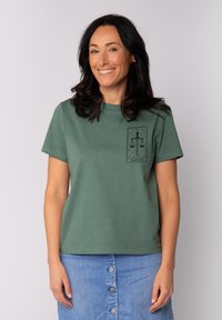 Groene katoenen T-shirt met een gedrukt ontwerp van schalen en het woord "JUSTITIE" in een rechthoekig kader op het linkerbovenbeen.