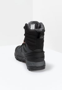 Black outdoor boot featuring a padded collar, textured fabric, rubber sole, and grey accents for improved grip and insulation.