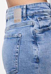Ανοιχτό μπλε τζιν παντελόνι με ψηλή μέση, με ορθογώνια ετικέτα PIECES, πίσω τσέπες και εμφανείς ραφές.