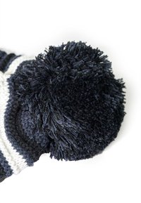 Black and white knitted beanie with a large textured black pom-pom on top. The material appears soft and thick, suitable for winter wear.
