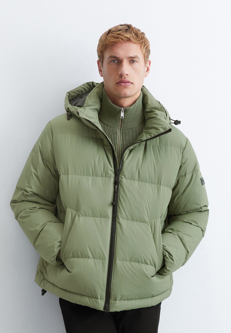 Veste rembourrée en olive verde mute, dotée d'une fermeture éclair à l'avant, d'une capuche ajustable et d'un col côtelé. Conçue en matériau doux et matelassé.