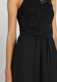Svart klänning med ett spetsliv och en flödande chiffonkjol. Har skulpterade spetskanter och en åtsittande topp med halterneck.