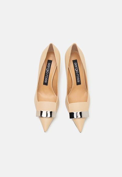 Beige pumps med spetstå som är gjorda av släta läder, med en bred rem med en glänsande silvermetallaccent över framdelen.