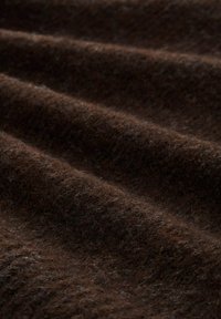 Bruine wollen stof met een zachte, getextureerde oppervlakte, met subtiele variaties in kleur en diepte, die zacht golvende plooien toont.