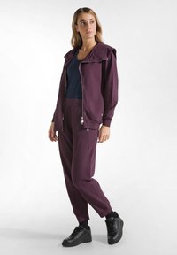 Lila zip-up jacka med huva, kombinerad med matchande lila joggingbyxor. Outfiten har en texturerad finish och kompletteras av svarta sneakers.