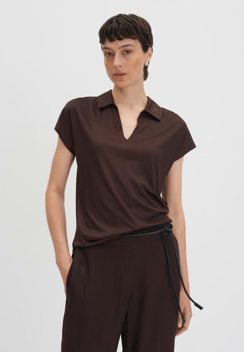 Polo shirt marrone a maniche corte con scollatura a V, realizzato in un tessuto morbido; abbinato a pantaloni marroni coordinati con una cintura in corda nera.