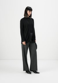 Svart ribbad cardigan över en svart topp, kombinerad med högmidjade grå vida byxor. Svarta spetsiga skor fulländar outfiten.