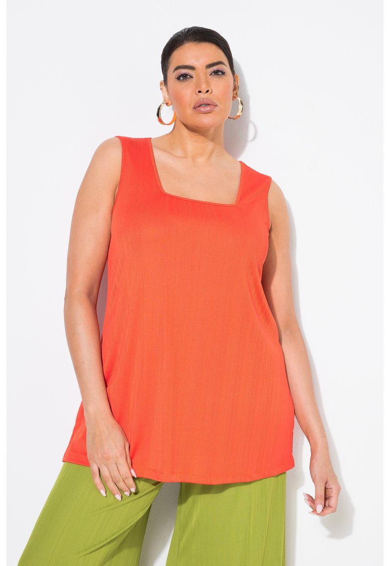 Top naranja sin mangas con escote cuadrado, con una textura acanalada, combinado con pantalones verdes de pierna ancha.