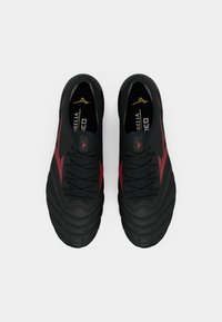 Černé a červené fotbalové kopačky Mizuno s tkaničkami, pohled shora na bílém pozadí.