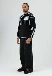 Zwart-wit gestreept shirt met lange mouwen, losvallende pasvorm, gecombineerd met zwarte jeans met wijde pijpen en zwarte schoenen met roze accenten.