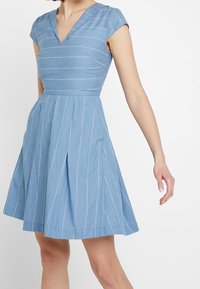 Blue striped dress featuring a V-neckline, cap sleeves, and a flared skirt with pleats; made from lightweight, textured fabric.