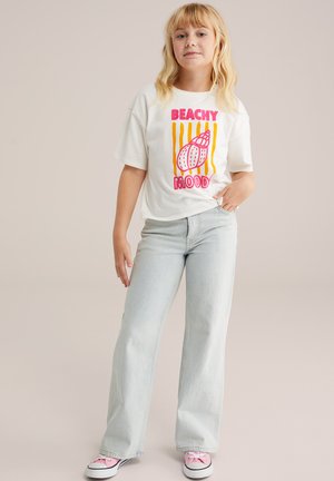 Camiseta blanca de algodón con estampado colorido de "BEACHY MOOD", combinada con jeans de pierna ancha de color azul claro y zapatillas rosas con detalles de lazo.