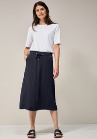 Gonna midi blu navy con vita elasticizzata e cordoncino, abbinata a una t-shirt bianca a girocollo. Indossata con sandali neri dal design flat. Tessuto morbido.