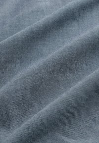 Textilstoff in hellblau, mit einer glatten, leicht strukturierten Oberfläche, feinen, subtilen Mustern und diagonalen Falten.