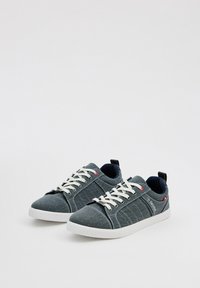 Zapatillas de tela gris con cordones blancos, interior en contraste color marino, lados texturizados y detalle del logo en el talón. Suela de goma, diseño casual.