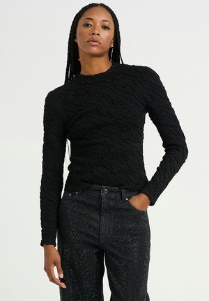 Black long-sleeve top with textured pattern, round neckline, paired with high-waisted dark jeans featuring embellishments.