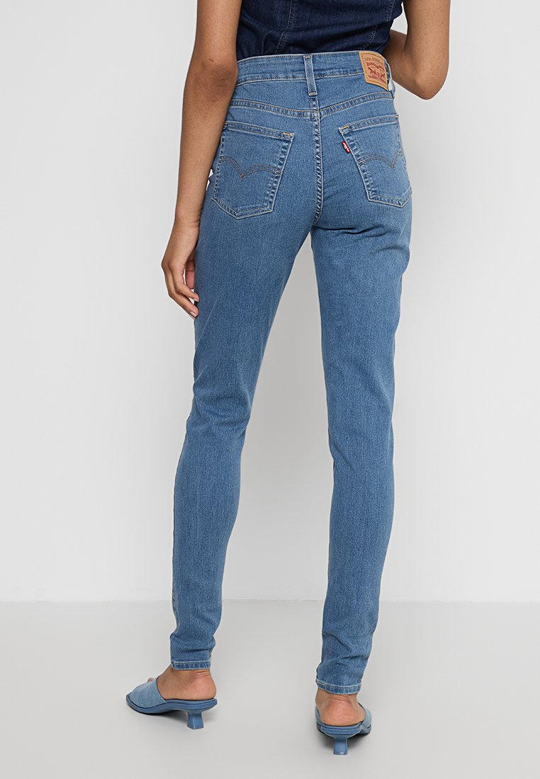 Jean en denim bleu clair avec une taille haute, coupe slim et deux poches arrière. Présente une étiquette à la taille et des détails de couture subtils.