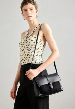 Sac à main noir présentant un mélange de textures lisses et en daim, un rabat avec une fermeture à boucle, et une longue bandoulière réglable.