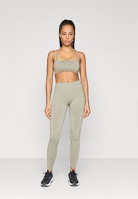 Φωτεινό ελαιόχρωμο αθλητικό σετ που περιλαμβάνει ένα cropped τοπ με ρυθμιζόμενες τιράντες και ψηλόμεσα κολάν, λεία υφή, συνδυασμένο με μαύρα αθλητικά παπούτσια.