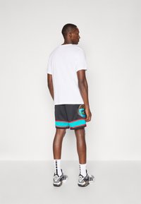 Sportbekleidung für Herren mit einem weißen T-Shirt, schwarzen Shorts mit türkisfarbenen und roten Akzenten sowie grafischen Details auf der Rückseite. Schwarz-weiße Sneakers.
