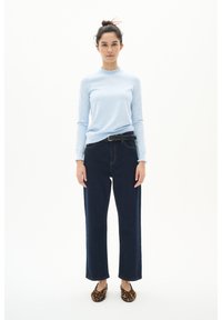 Light blue long-sleeve top with ruffled neckline, dark blue high-waisted jeans with straight legs, and animal print flats.