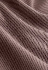 Rippenstoff in einem gedämpften Mauve-Ton, mit einer weichen, strukturierten Oberfläche und feinen horizontalen Linien, die seine Dehnbarkeit und Sanftheit zur Geltung bringen.