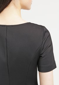 Sort kjole med korte ærmer, glat materiale, rund halsudskæring og diskrete stikninger på ryggen.