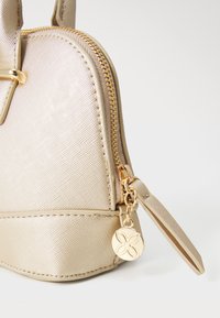 Petit sac à main en or avec une finition texturée, doté d'une fermeture éclair et de quincaillerie dorée. Comprend un charme décoratif sur le côté.