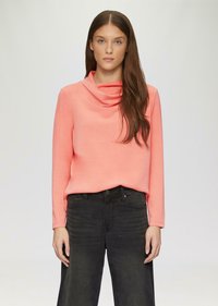 Bluzka z kapturem, z długim rękawem w jasnym koralowym kolorze, wykonana z miękkiego materiału, zestawiona z czarnymi jeansami o wysokim stanie. Minimalistyczny design, gładka tekstura.