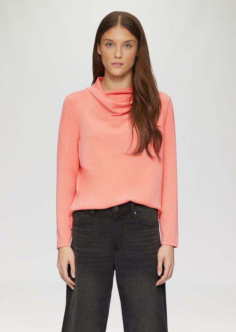 Bluzka z kapturem, z długim rękawem w jasnym koralowym kolorze, wykonana z miękkiego materiału, zestawiona z czarnymi jeansami o wysokim stanie. Minimalistyczny design, gładka tekstura.