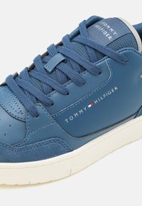 Sininen nahkainen lenkkari, jossa on verkko-osia, pyöreä kärki ja valkoinen kumipohja. Sivussa on Tommy Hilfiger -logo ja kontrastiväriset nauhat.