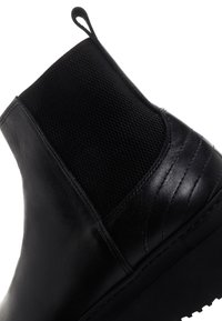 Bottine en cuir noir avec panneau élastique sur le côté, languette à l'arrière et semelle compensée avec un relief texturé.