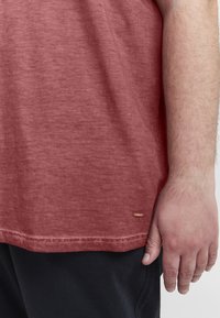 Maronfarvet kortærmet t-shirt i blødt, tekstureret stof. Har en diskret kant og et lille mærkelogo nederst til venstre.
