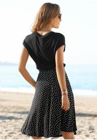 Schwarzes kurzärmliges Oberteil kombiniert mit einem ausgestellten schwarzen Rock mit weißen Pünktchen. Das Outfit wird durch ein dekoratives Armband ergänzt.