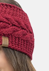Diadema roja de punto con un patrón texturizado y una etiqueta tejida. El diseño presenta un aspecto grueso y trenzado. Material suave y cálido.