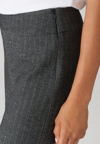 Pantalons met een zwart-wit houndstooth patroon en een zijrits, met een gladde textuur en een op maat gemaakte pasvorm. Close-up van het taillegebied.