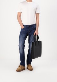 Vit t-shirt med kort ärm, blå denimjeans, bruna skor, håller en svart läder tote-väska med två handtag. Avslappnad outfit.