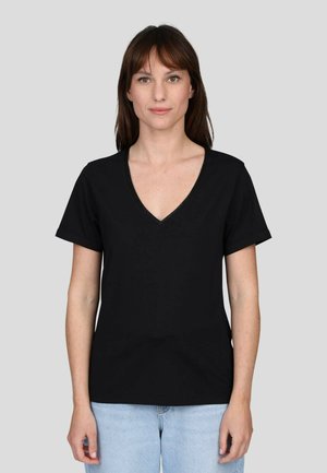 T-shirt noir à col en V, fabriqué en tissu doux, avec des manches courtes et une coupe décontractée. Porté avec un jean bleu clair, sur fond uni.