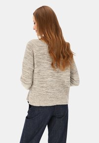 Jasnoszary sweter dzianinowy o fakturowanym wykończeniu, z luźnym krojem i opuszczonymi ramionami, zestawiony z niebieskimi spodniami dżinsowymi.