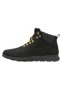 Botas de tobillo de ante negro con ojales dorados, cordones naranjas, tela negra texturizada en el cuello y una suela gruesa de goma.