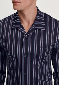 Marineblauwe gestreepte blouse met verticale strepen in wit en lichtpaars, voorzien van een knoopsluiting aan de voorkant, een korte kraag en een borstzak.