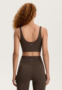 Barna sportmelltartó és magas derekú leggings sima anyagból, diszkrét logóval a hátsó részen és testhezálló fazonnal.