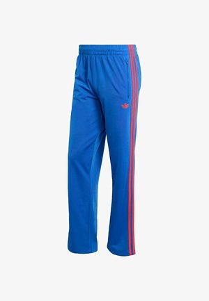 Blaue Sporthose aus synthetischem Stoff. Mit roten Streifen an den Seiten und einem elastischen Bund. Mit Reißverschlusstasche.