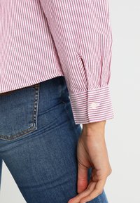 Gros plan d'une personne portant un jean en denim bleu et une chemise à manches longues rayée rouge et blanc avec un poignet boutonné.