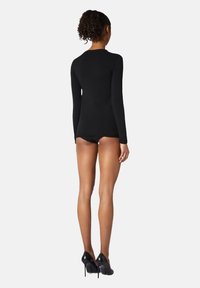 Svart långärmad topp gjord av stretchtyg, figurnära design, slät textur. Matchas med svarta trosor och högklackade skor.